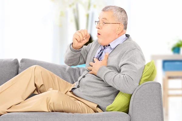 Человек кашляет, сидя на диване — стоковое фото