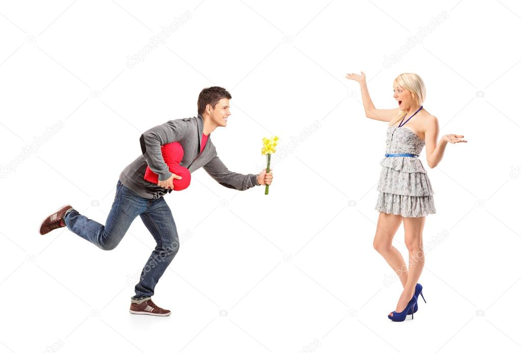 Boyfriend in love running with flowers and heart shape object towards his excited girlfriend