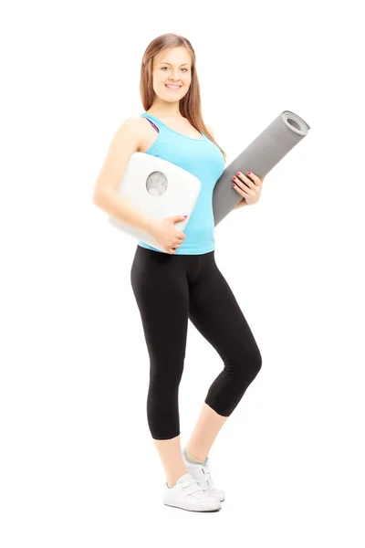 Female athlete holding weight scale and mat — Stock Photo, Image