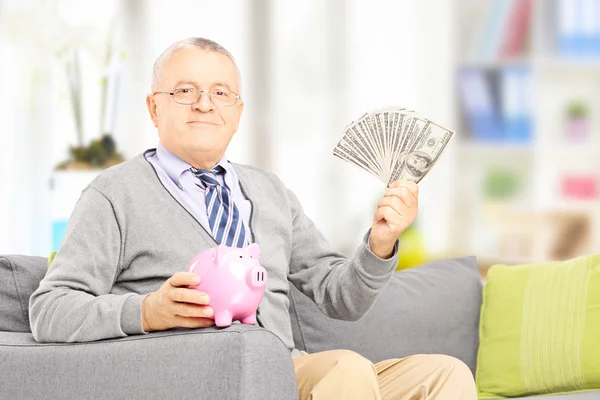 Sénior segurando um banco porquinho e dinheiro — Fotografia de Stock