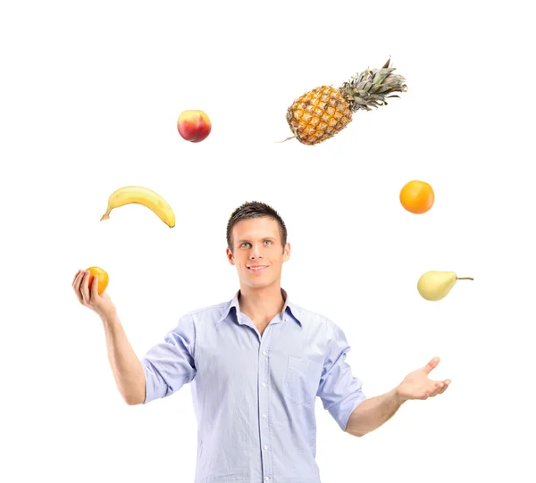 Hombre guapo sonriente haciendo malabarismos con frutas —  Fotos de Stock