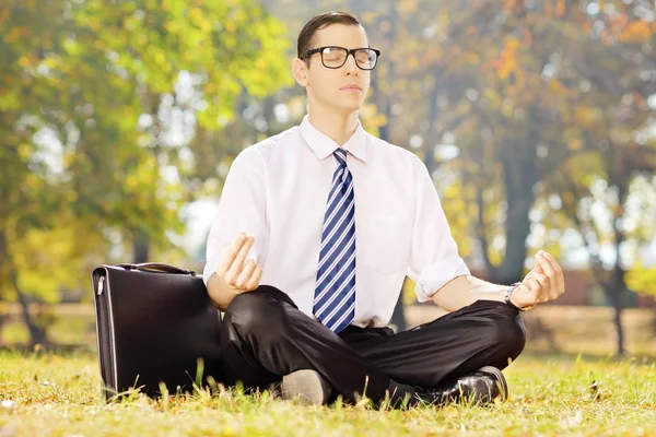 Young businessperson seated on a grass meditating in a park — Stock Photo, Image