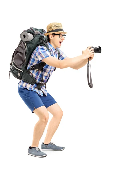 Ganzkörperporträt eines männlichen Touristen mit Rucksack, der ein Foto mit seiner Kamera auf weißem Hintergrund macht — Stockbild Männlicher Tourist beim Fotografieren — Stockfoto