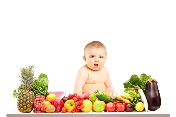 Bambino seduto su un tavolo pieno di frutta e verdura diverse — Foto Stock