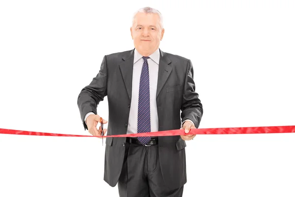 Mature businessman cutting red tape — Stock Photo, Image