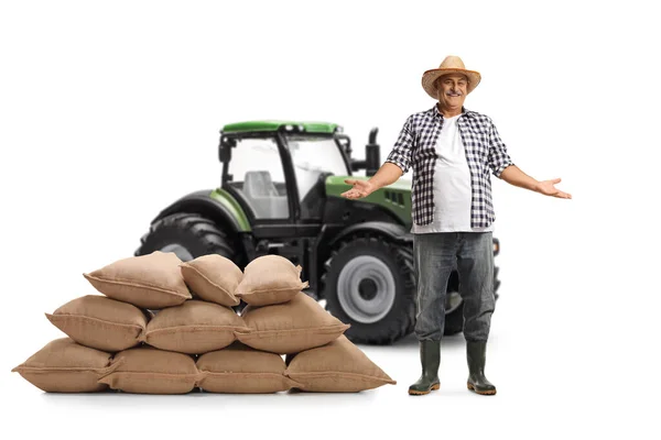 一个头戴草帽的成熟农民的全长肖像 在一辆白色背景的拖拉机前展示了一堆麻袋 — 图库照片