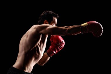 Siyah arka planda boks eldivenleriyle yumruk atan güçlü bir genç adam.