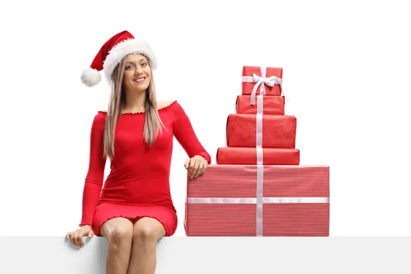 サンタの帽子をかぶったブロンドの女性と白い背景に孤立したプレゼントとパネルに座って — ストック写真