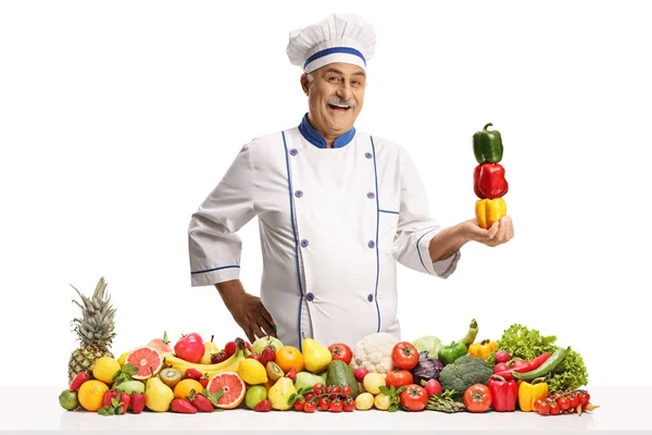 笑着的男厨师拿着甜椒在一堆白色背景的水果和蔬菜后面 — 图库照片