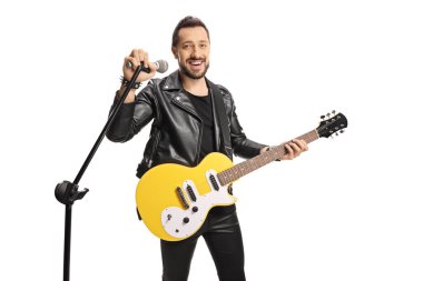 Elektro gitarlı bir erkek rock yıldızı beyaz arka planda izole edilmiş bir mikrofonda şarkı söylüyor.