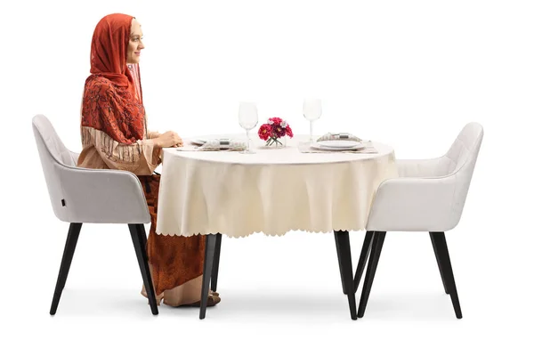 ヒジャーブを着た若い女性のプロフィール写真白地に隔離されたレストランのテーブルに座って — ストック写真