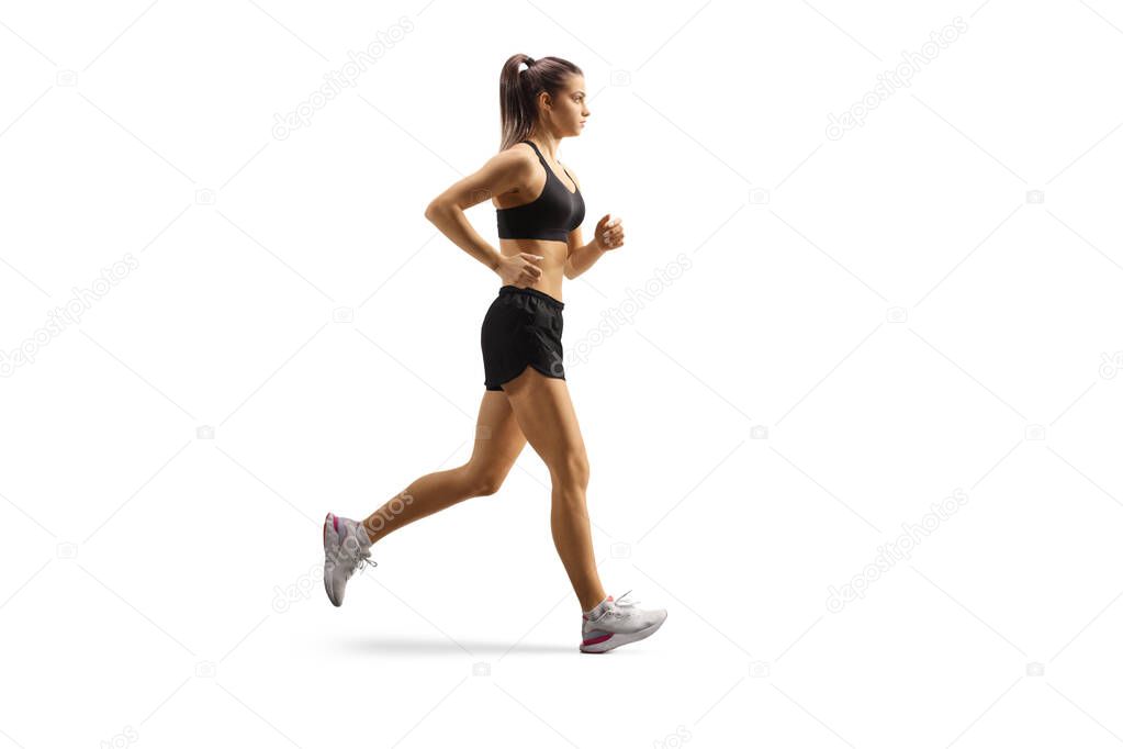 Full length profile shot of a female athlete wearing crop top and shorts and running isolated on white background
