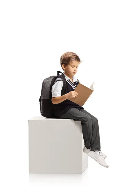 Schoolboy Sentado Cubo Branco Lendo Livro Isolado Fundo Branco — Fotografia de Stock