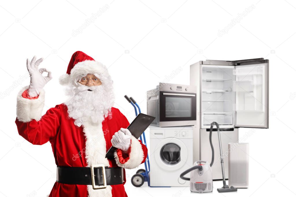 Santa claus holding a clipboard and gesturing a good sign in front of home appliances isolated on white background