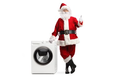 Noel Baba 'nın tam boy portresi çamaşır makinesine yaslanıyor ve beyaz arka planda izole edilmiş baş parmaklar veriyor. 