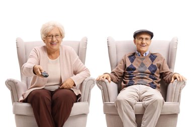 Yaşlı çift bir koltukta oturuyor ve ellerinde beyaz arka planda izole edilmiş bir televizyon kumandası var.