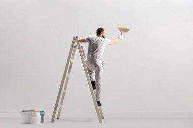 Beyaz arka planda izole edilmiş bir merdivene duvar boyayan bir ressamın arka görüntüsü