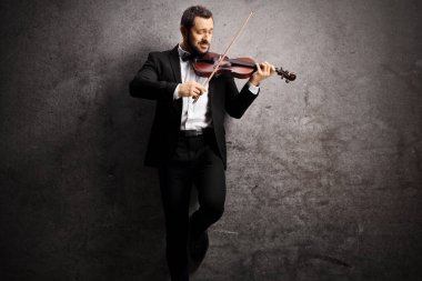 Zarif genç adam keman çalıyor ve gri engebeli bir arka plana yaslanıyor.