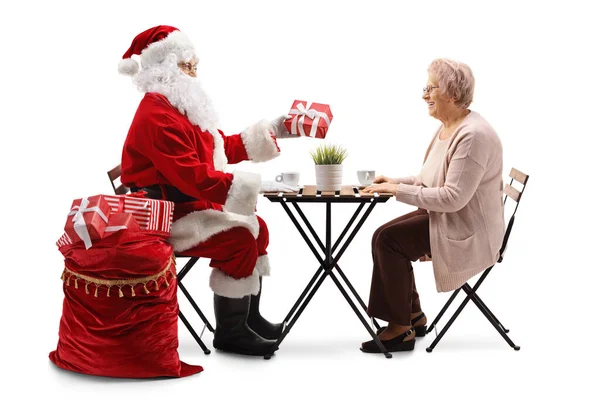 Święty Mikołaj Siedzi Przy Stole Daje Prezent Świąteczny Starszej Pani — Zdjęcie stockowe