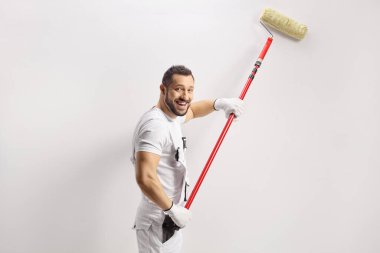 Gülümseyen boyacı bir duvar boyuyor ve beyaz arka planda izole edilmiş kameraya bakıyor.