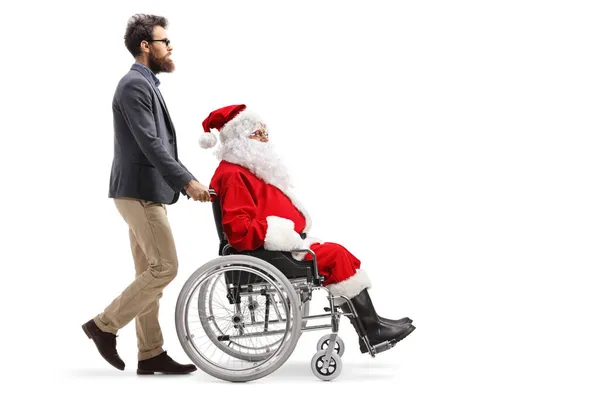 白い背景に隔離された車椅子でサンタを押している男の完全な長さのプロフィールショット — ストック写真