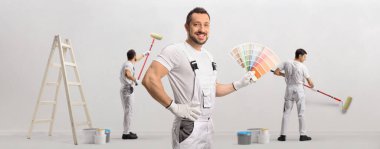 Bir renk paleti tutan ressam ve diğer ressamlar beyaz arkaplana izole bir duvar çiziyorlar