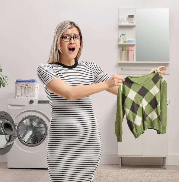 Kızgın genç bir kadın banyoda küçülmüş bir bluz tutuyor. 