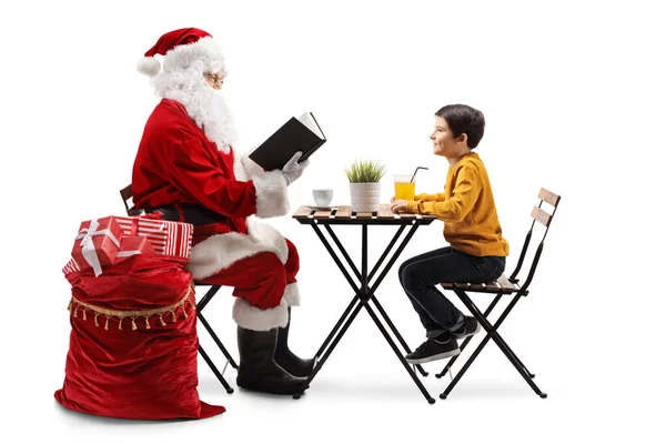 Święty Mikołaj Siedzi Przy Stole Czyta Książkę Chłopcu Odizolowanemu Białym — Zdjęcie stockowe
