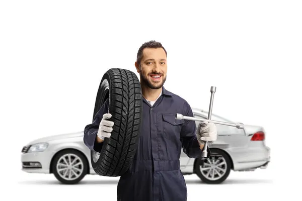 汽车修理工站在一辆拖着轮胎的银色汽车前面 还有一个白色背景的扳手 — 图库照片