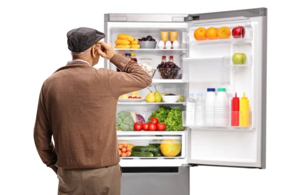 白い背景に隔離された食べ物を持つオープン冷蔵庫を見ている高齢者の後ろのビューショット — ストック写真