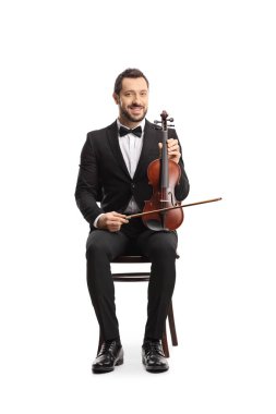 Genç, zarif bir adam bir sandalyede oturuyor ve elinde beyaz arka planda izole edilmiş bir keman tutuyor. 