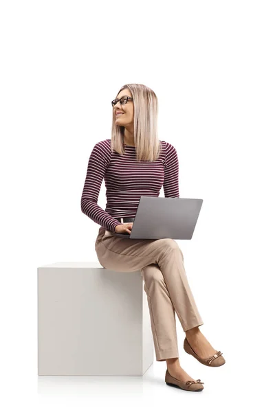 若い女性が白いキューブの上にノートパソコンで座って白い背景に隔離された後ろを見る — ストック写真