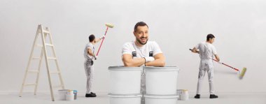 Ev dekoratörleri duvar boyuyor ve bir ressam beyaz arka planda izole edilmiş kovalara yaslanıyor.