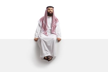 Suudi Arabistan 'lı adam boş bir panelde oturuyor ve beyaz arka planda izole edilmiş kameraya bakıyor.