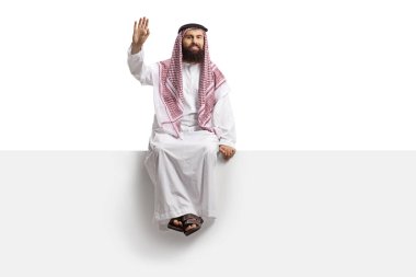 Suudi Arabistan 'lı adam boş bir panelde oturuyor ve beyaz arka planda izole edilmiş kameraya el sallıyor.