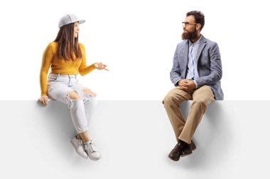 Genç bir kadın ve sakallı bir adam boş bir panelde oturup beyaz arka planda izole edilmiş bir şekilde sohbet ediyorlar.