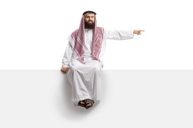 Suudi Arabistan 'lı adam boş bir panelde oturuyor ve beyaz arka planda izole edilmiş bir yeri işaret ediyor.