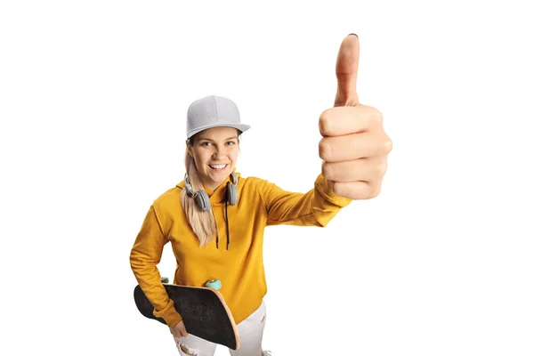带着耳机和滑板的女青少年在白色背景的摄像机前展示一个大拇指向上的标志 — 图库照片