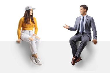 Takım elbiseli ve kravatlı bir adam beyaz arka planda boş bir panelde oturan genç bir kızla konuşuyor.