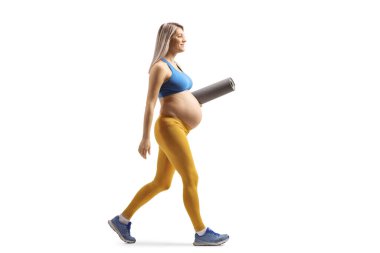 Spor kıyafetli hamile bir kadının beyaz arka planda izole edilmiş egzersiz paspası taşırken tam boy profil fotoğrafı.