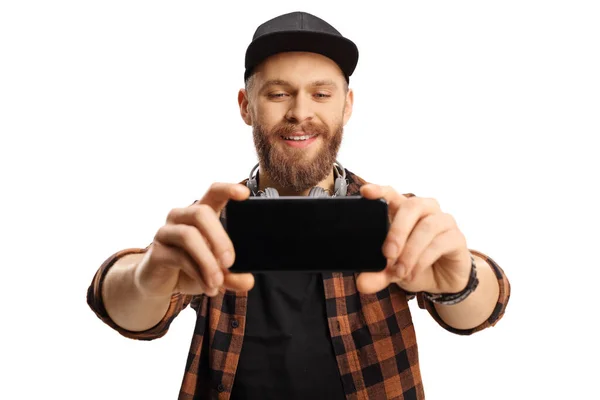 髭を生やした流行の男が白い背景に隔離されたスマートフォンで自撮り写真を撮る — ストック写真
