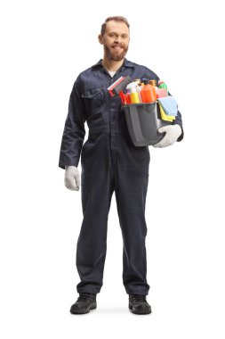Full length portrait of a male cleaner in a uniform holding a bucket of cleaning supplies and smiling isolated on white background