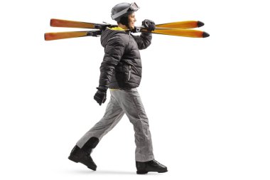 Full length profile shot of a man with skiing boots walking and carrying skis isolated on white background