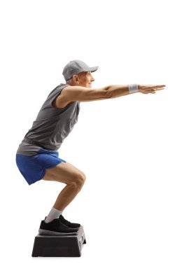 Full length profile shot of an elderly man working out on a step aerobic platform isolated on white background