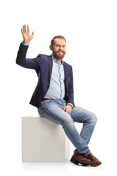 Young Man Suit Jeans Sitting White Cube Waving Isolated White — Stockfoto