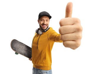 Sarı tişörtlü, kaykaylı mutlu adam beyaz arka planda parmaklarını kaldırıyor.