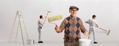 Elinde boya silindiri, renkli kova ve profesyonel boyacı tutan sıradan yaşlı bir adam.