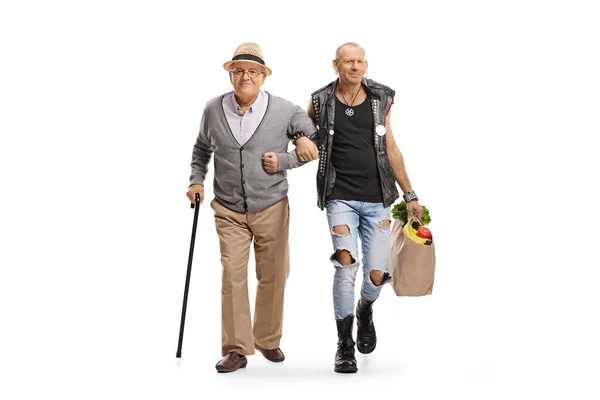 一个庞克帮一个拿着手杖提着用白色背景隔开的购物袋的老人的全长肖像 — 图库照片