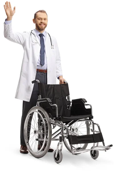 車椅子の後ろに立って白い背景に孤立して手を振る若い男性医師 — ストック写真