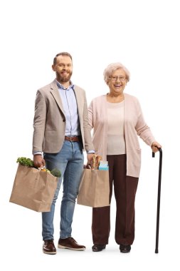 Genç bir adam yaşlı bir kadına yardım ediyor ve beyaz arka planda izole edilmiş alışveriş torbaları tutuyor.